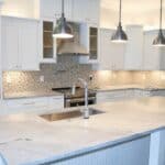 A white modern kitchen with hanging lights, a modern faucet and sink
